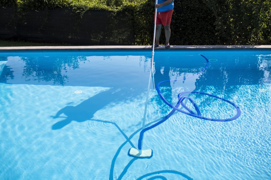 Male pool cleaner cleaning a blue pool - Puravida Pools 